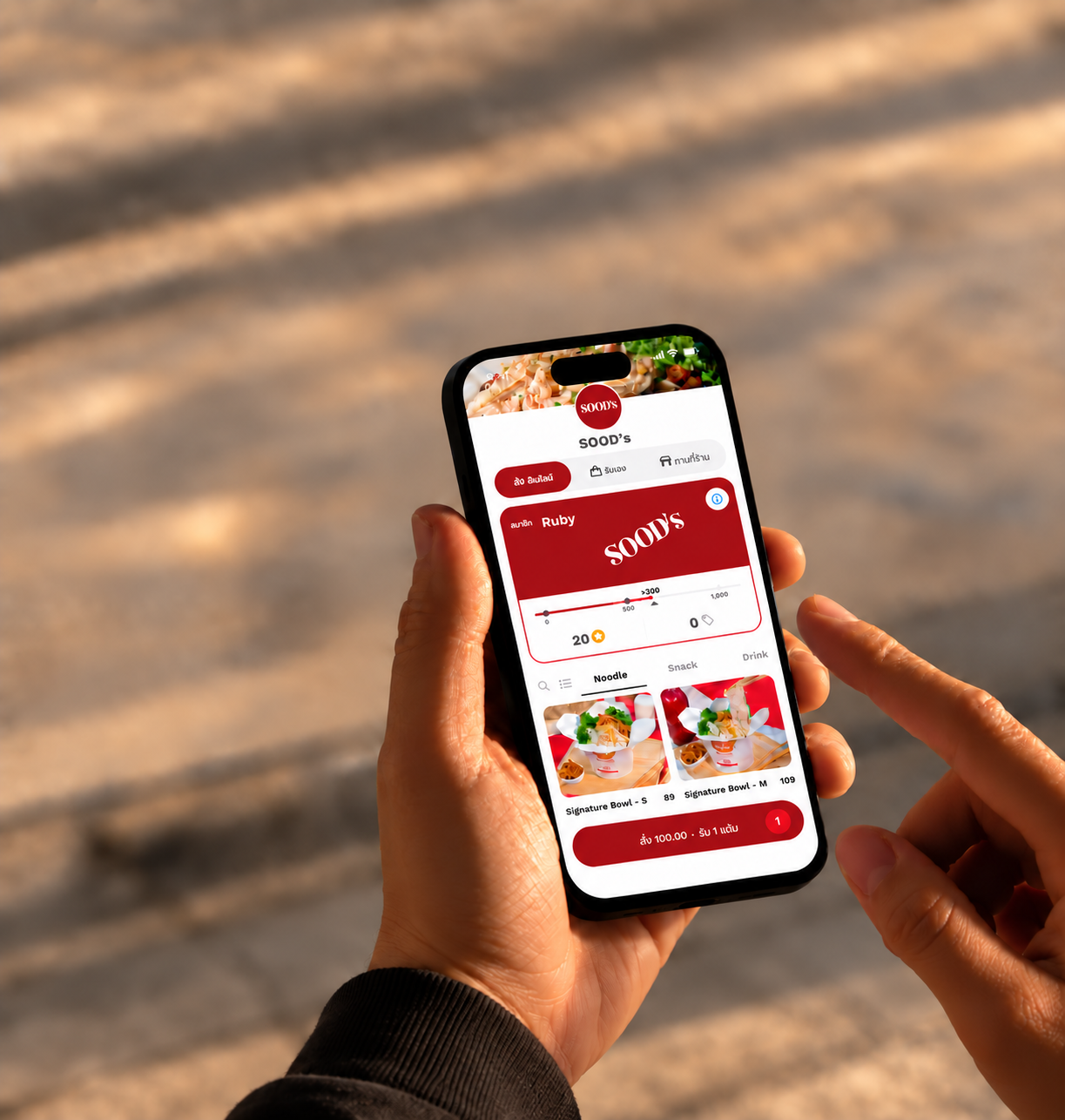 A customer holding a phone with the SOOD’s DotDash ordering and rewards screen